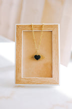 Gold necklace with a heart pendant on a wooden display box against a beige background