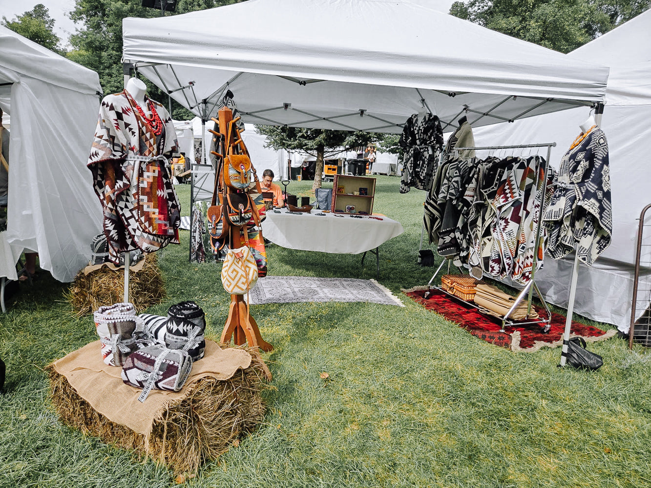 Outdoor market stall with clothing and accessories on display under a white tent.